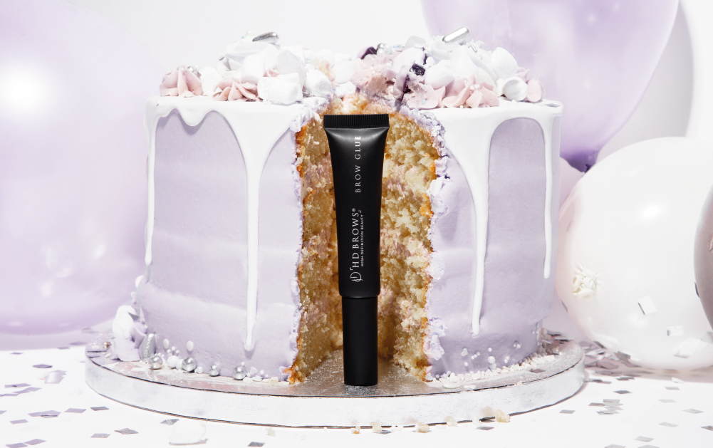Tube of Brow Glue stood in front of a birthday cake